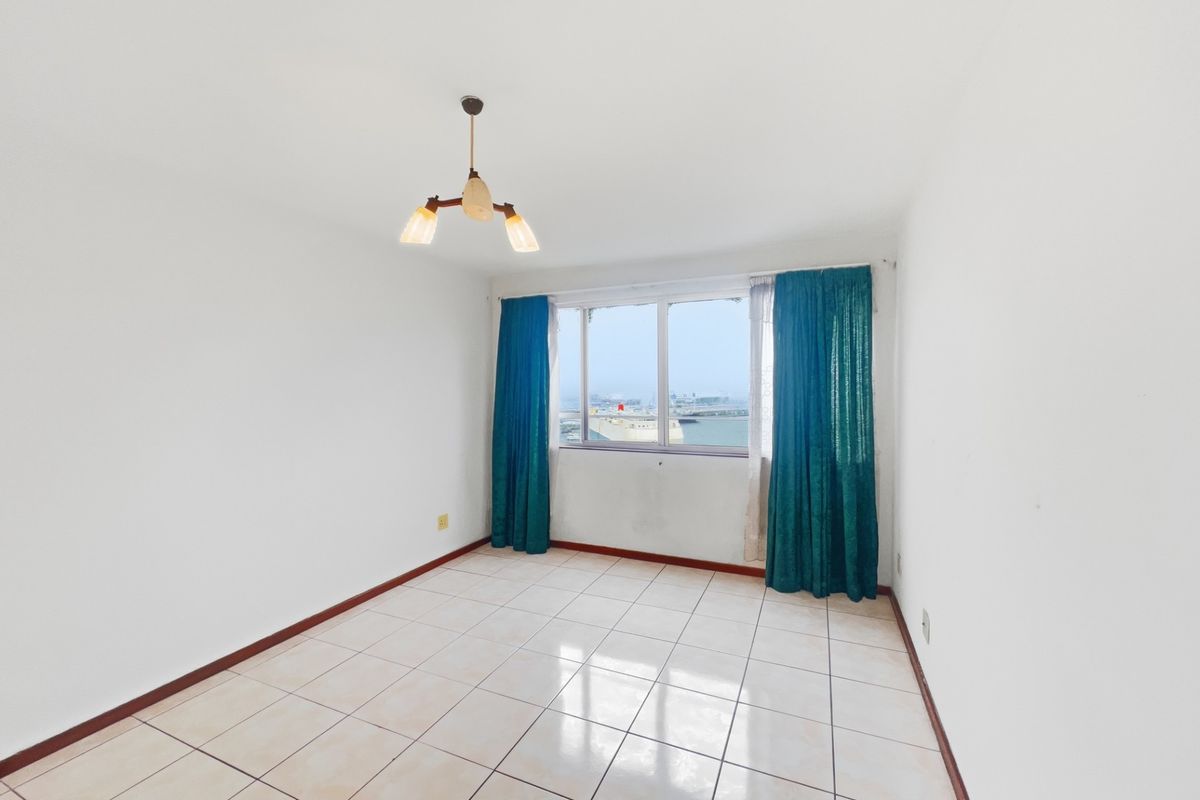 A bright, empty bedroom featuring tiled flooring, neutral walls, and a window with views, providing a blank canvas for personalization.