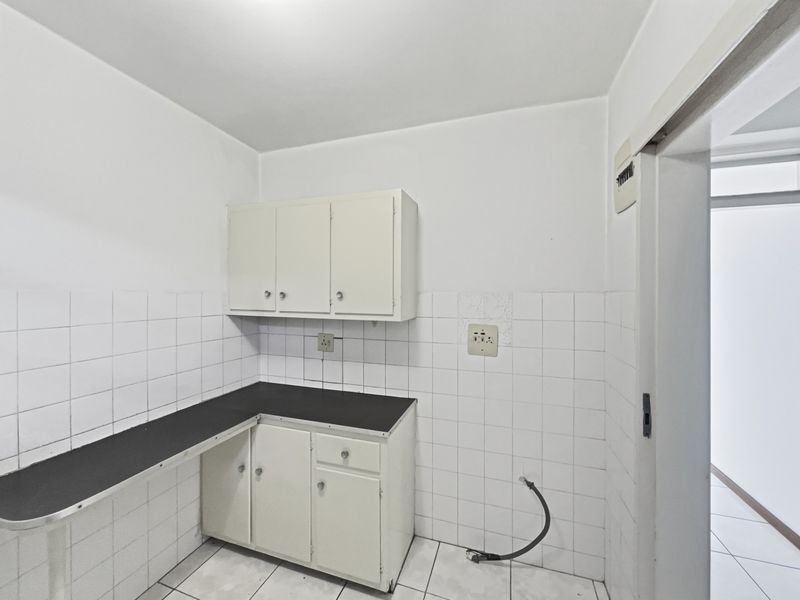 A functional scullery area featuring built-in cabinetry, laminate countertops, and tiled surfaces, offering a practical space for utility and preparation tasks.