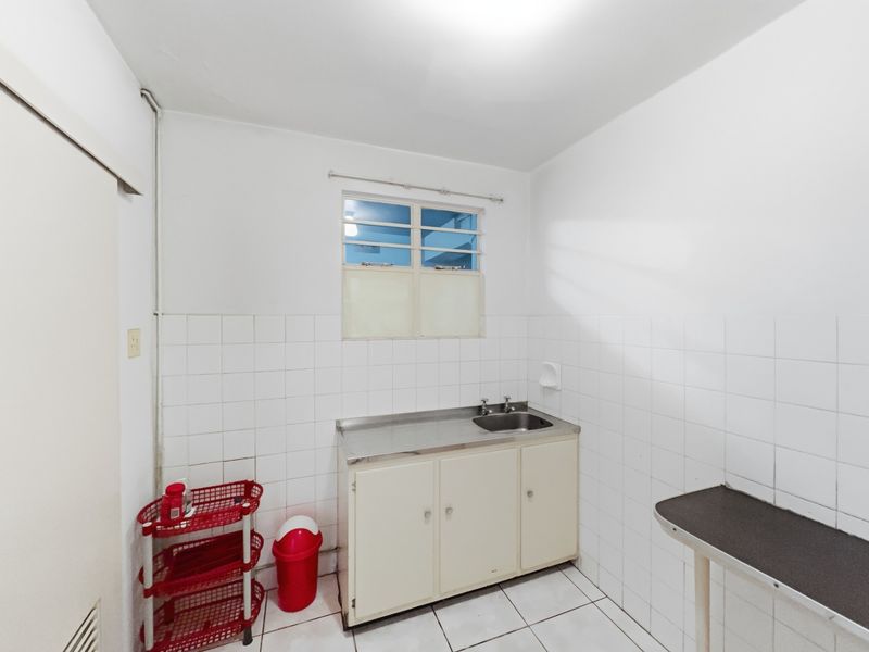 A functional laundry room featuring a stainless steel sink, built-in cabinetry, tiled splashback, and tiled flooring.