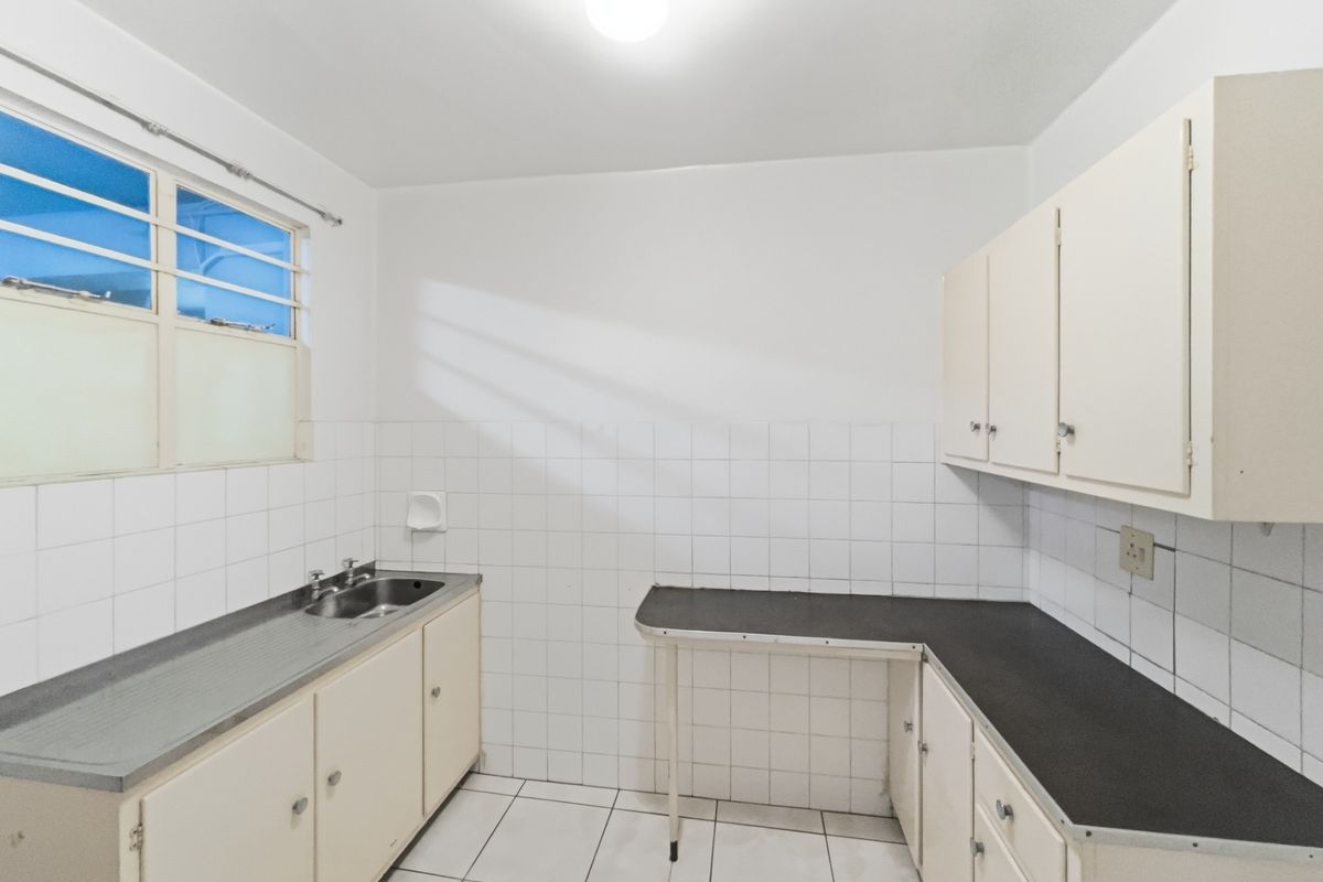 A functional, empty kitchen featuring tiled splashbacks, laminate countertops, and built-in cabinetry, offering a blank canvas for modern renovation.