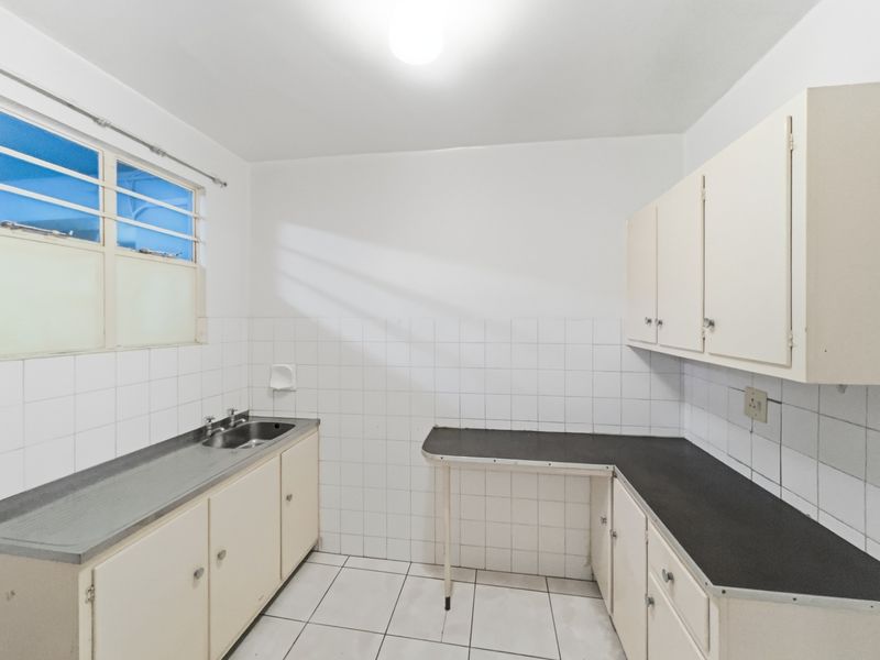 A functional, empty kitchen featuring tiled splashbacks, laminate countertops, and built-in cabinetry, offering a blank canvas for modern renovation.
