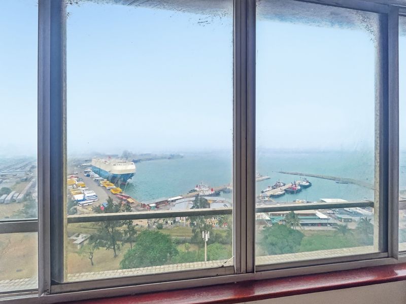 A view from an interior window overlooking a busy industrial harbor with ships and port infrastructure.