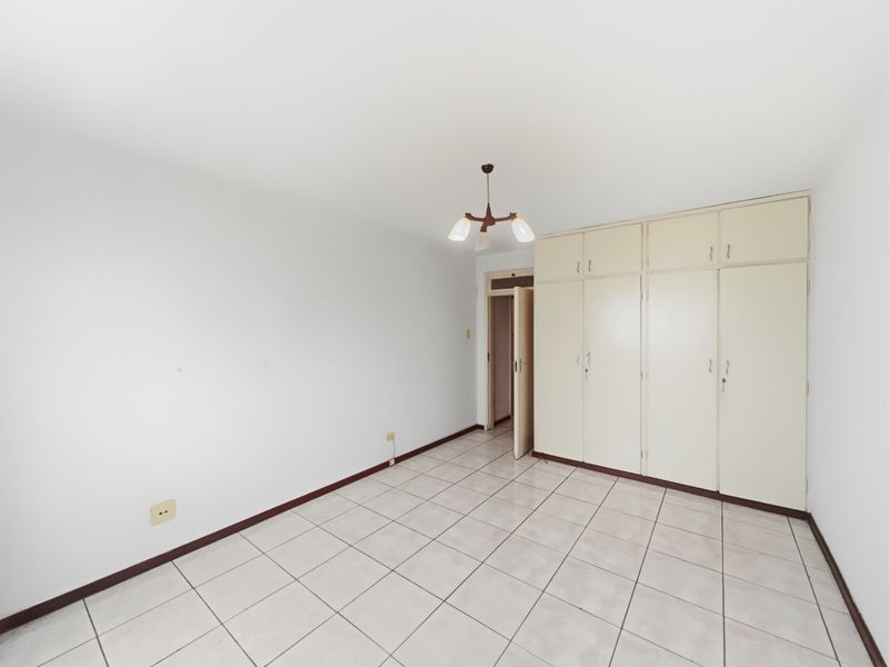 A clean, empty bedroom featuring neutral tiled flooring and extensive built-in cupboard storage, offering a blank canvas for personalization.