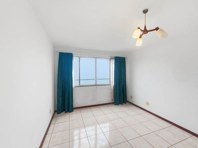 A vacant bedroom featuring neutral tiled flooring, a central ceiling light fixture, and a window with views, ready for personalization.