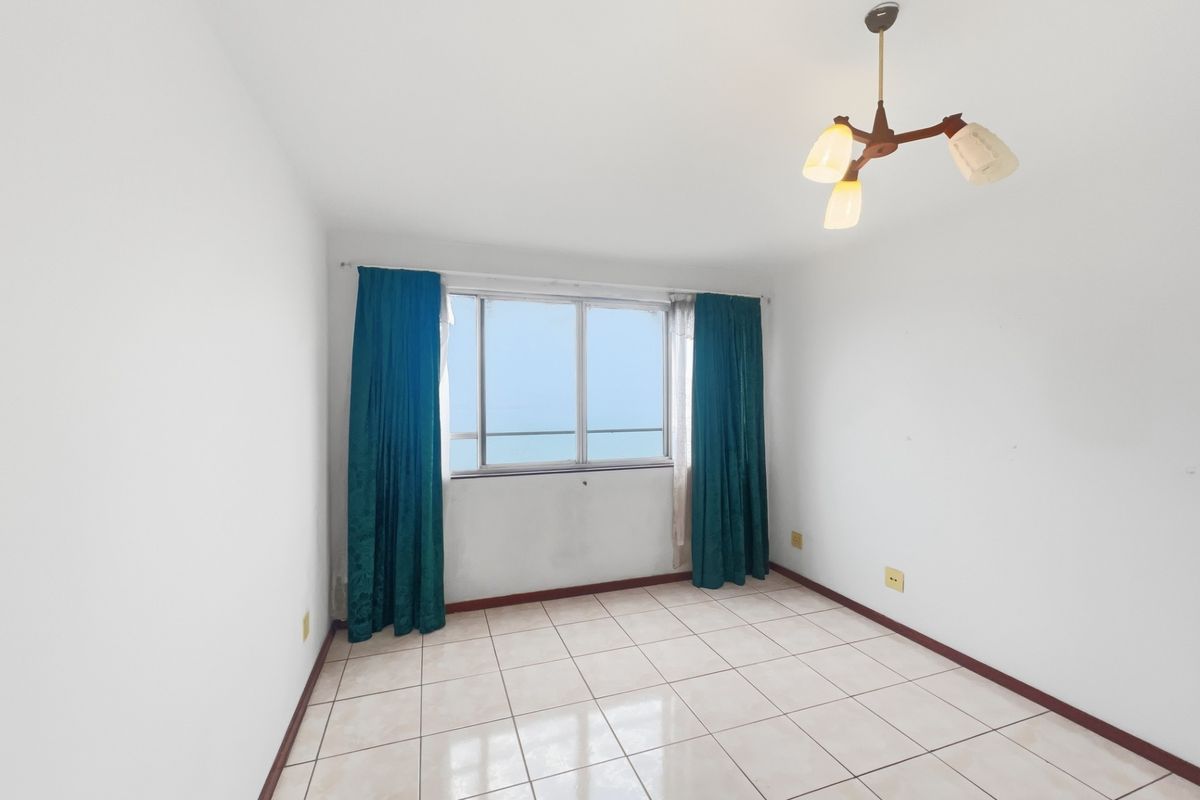 A vacant bedroom featuring neutral tiled flooring, a central ceiling light fixture, and a window with views, ready for personalization.