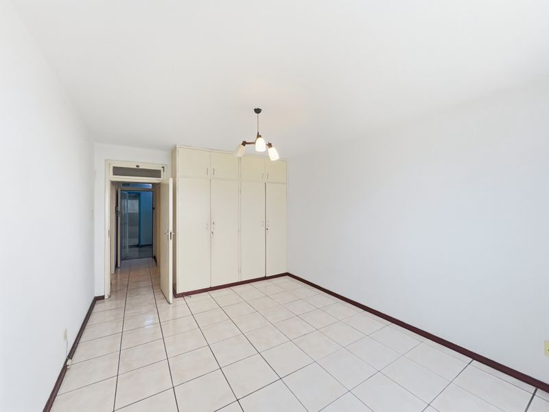 A clean, empty bedroom featuring neutral tiled flooring and ample built-in cupboard storage space.