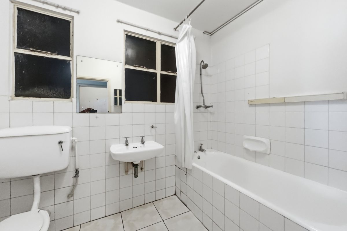 A functional bathroom featuring a bathtub with shower mixer, wall-mounted basin, and toilet with high-level cistern, finished with white wall and floor tiles.