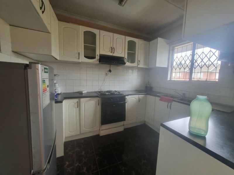 A functional kitchen featuring built-in cabinetry, a hob, oven, extractor fan, and tiled backsplash, offering potential for modernization and aesthetic updates.
