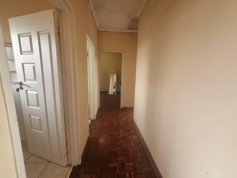A functional hallway featuring traditional parquet flooring and access to multiple rooms, requiring cosmetic updates to improve the overall aesthetic.