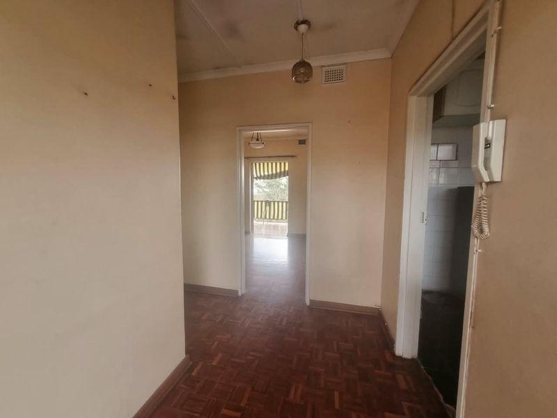 A vacant hallway featuring original parquet flooring and an intercom system, leading through to an adjacent living area.
