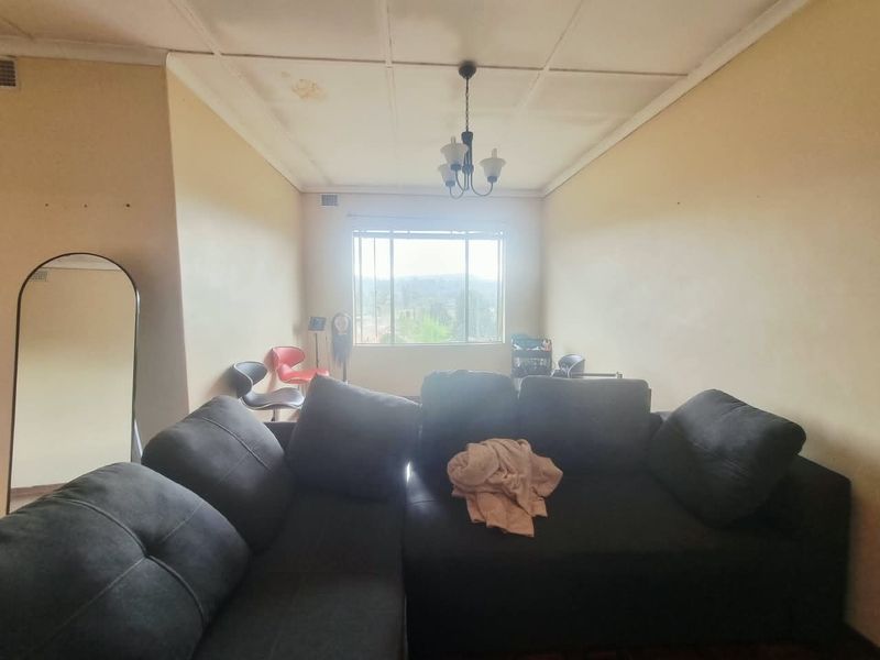 A living room featuring a large window, ceiling tiles with visible water staining, and a central hanging light fixture.