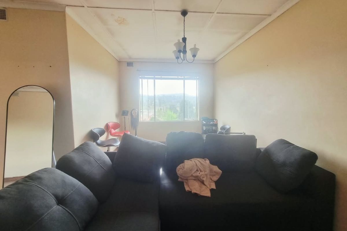 A living room featuring a large window, ceiling tiles with visible water staining, and a central hanging light fixture.
