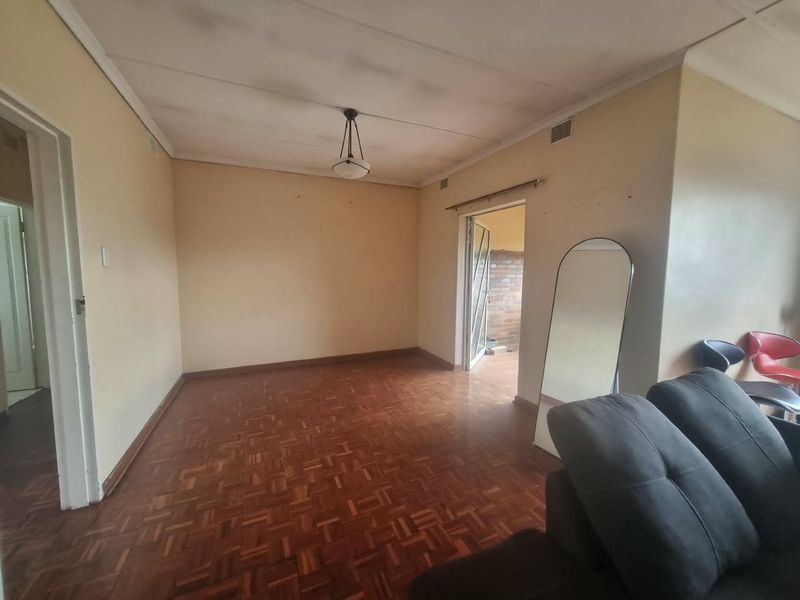 A living room featuring traditional parquet flooring and a ceiling light fixture, requiring cosmetic updates to the walls and ceiling.