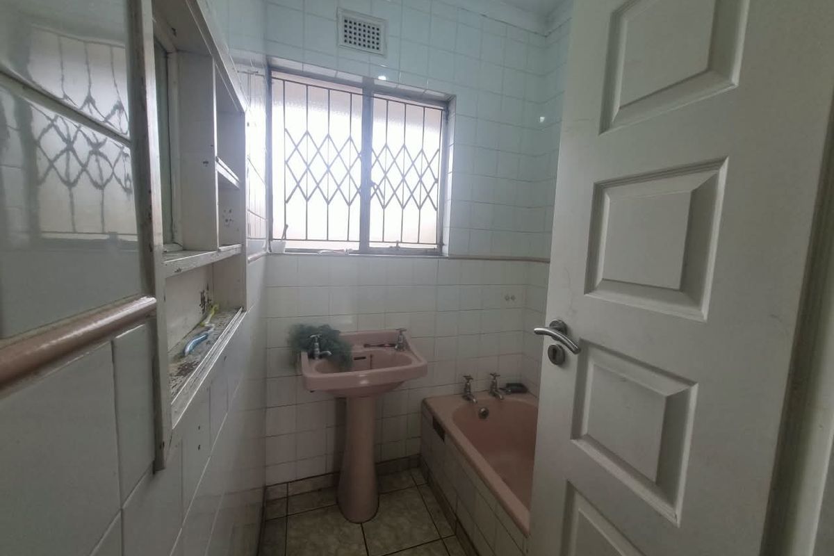 A dated bathroom featuring a pink pedestal basin and bathtub, tiled walls, and a security gate on the window.