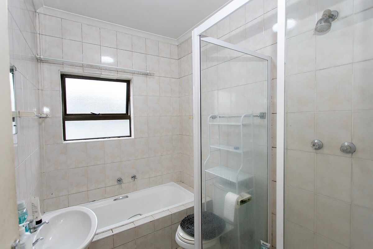 A functional bathroom featuring a built-in bathtub, separate shower enclosure, and wall-mounted basin with neutral tiled finishes.