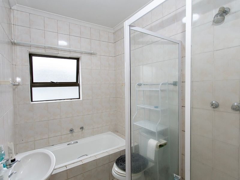 A functional bathroom featuring a built-in bathtub, separate shower enclosure, and wall-mounted basin with neutral tiled finishes.