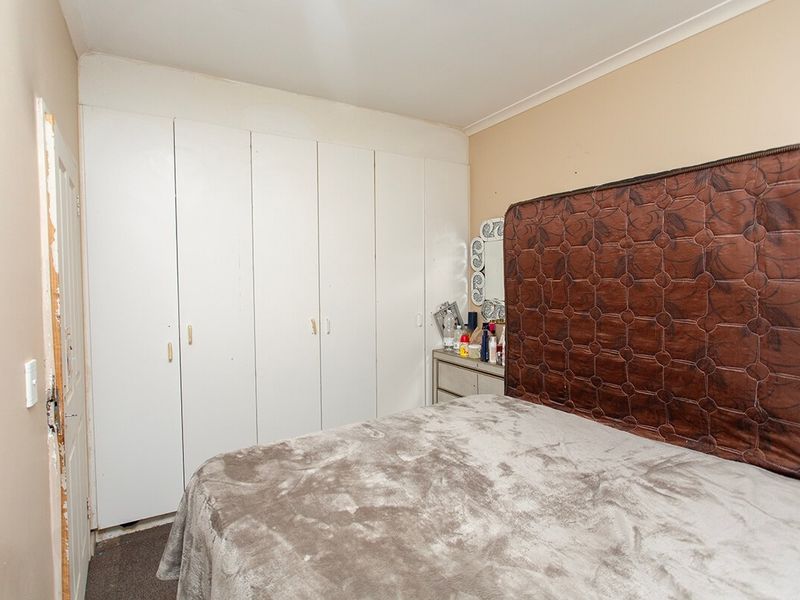 A bedroom featuring built-in cupboards and carpet flooring, requiring some cosmetic updates to the door frame and wall finishes.