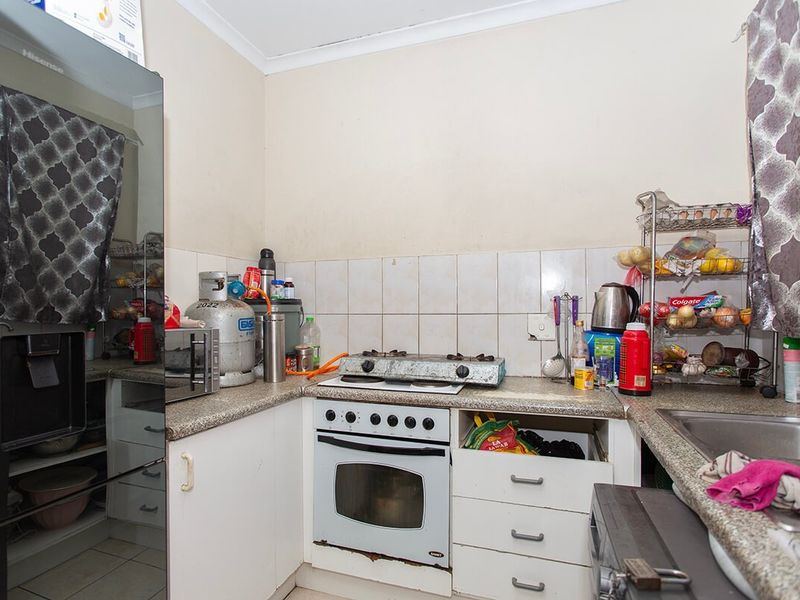 Compact kitchen featuring built-in oven, gas hob, laminate countertops, and tiled backsplash, requiring some maintenance and cosmetic updates to improve functionality and aesthetic appeal.