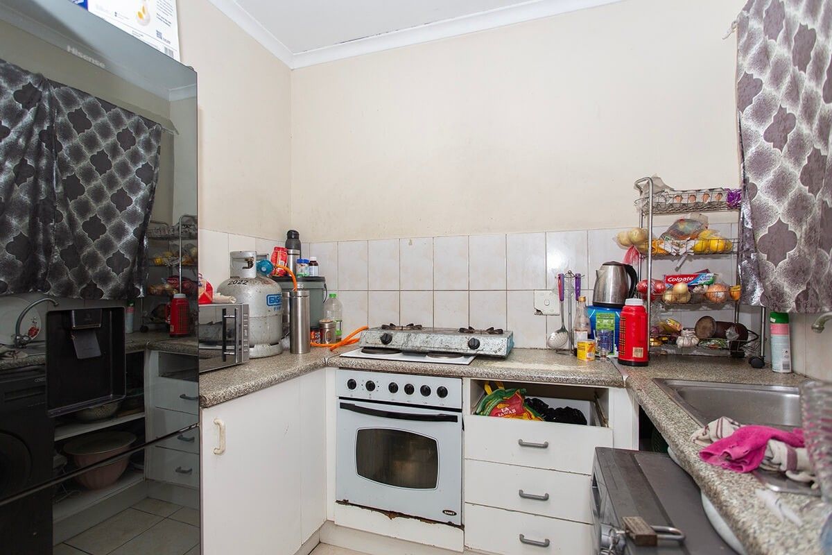 Compact kitchen featuring built-in oven, gas hob, laminate countertops, and tiled backsplash, requiring some maintenance and cosmetic updates to improve functionality and aesthetic appeal.