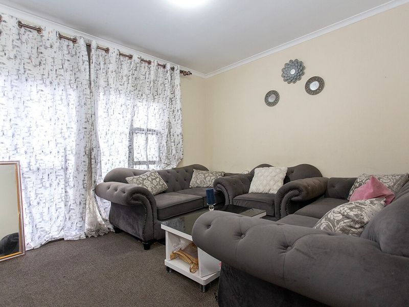 A comfortable living room featuring neutral walls, carpeted flooring, and a large sliding glass door with curtains providing natural light.