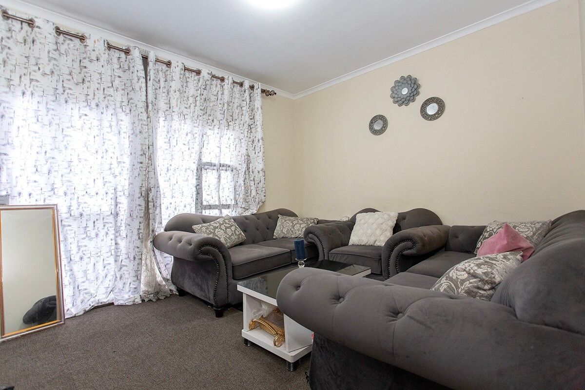 A comfortable living room featuring neutral walls, carpeted flooring, and a large sliding glass door with curtains providing natural light.