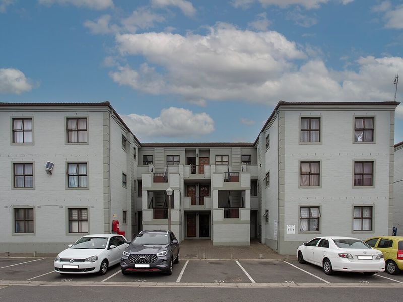 Front elevation of a multi-story apartment complex featuring paved parking bays and external access staircases.