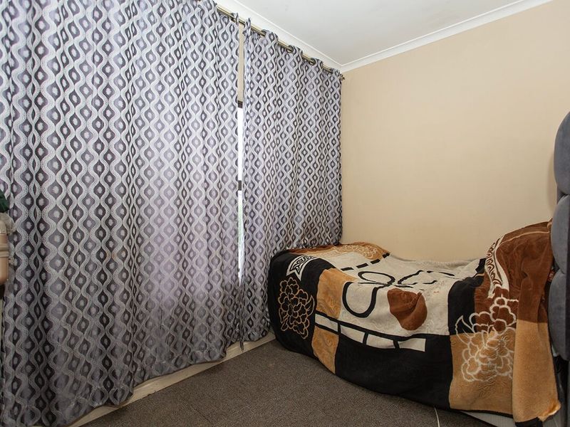 A compact bedroom featuring carpeted flooring and a window dressed with patterned curtains.
