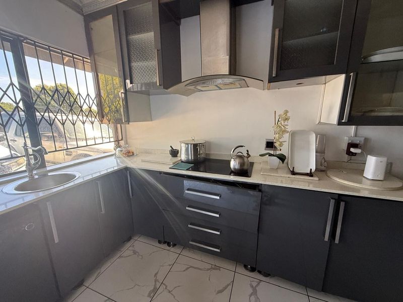A compact kitchen featuring dark grey cabinetry, stone countertops, an electric hob with extractor fan, and tiled flooring.