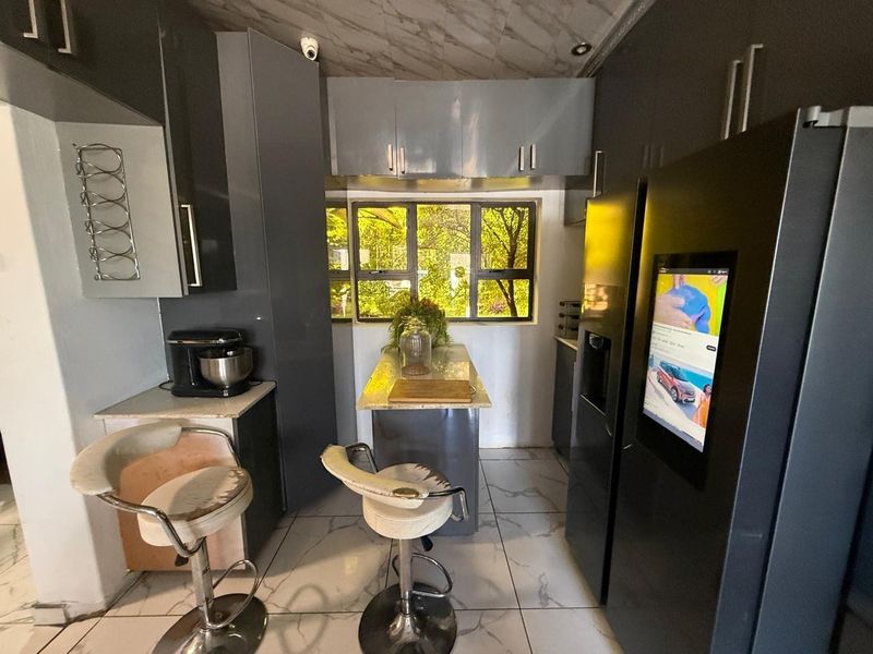 Compact kitchen featuring dark grey built-in cabinetry, a central island with stone countertop, and tiled flooring with natural light from the window.