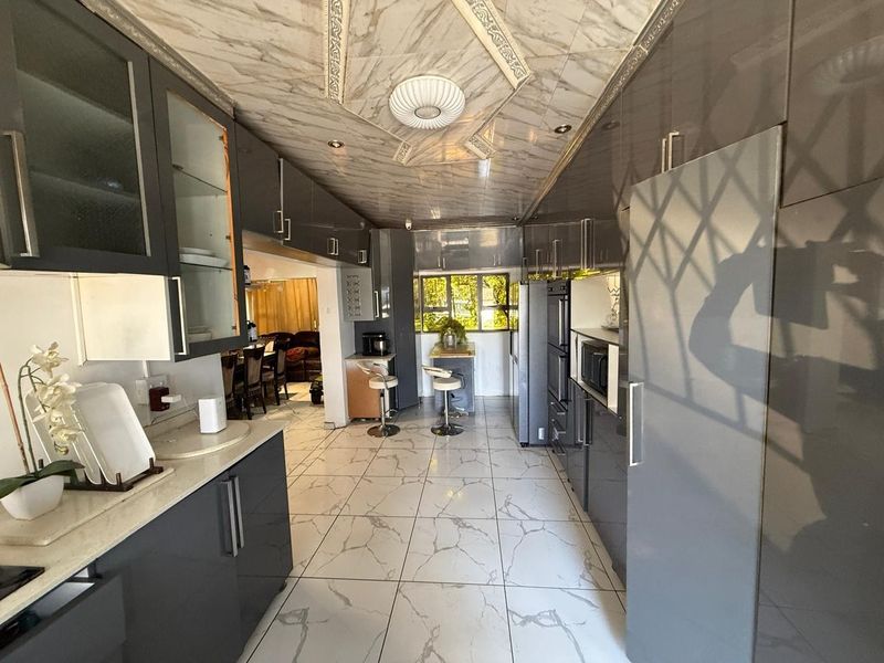 Modern kitchen featuring high-gloss cabinetry, stone countertops, integrated appliances, and distinctive marble-effect tiled flooring and ceiling finishes.