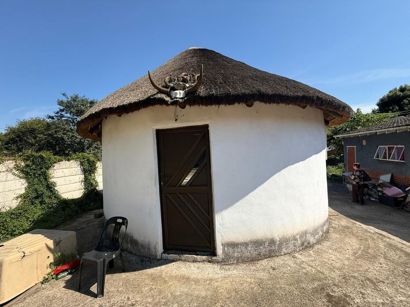 A traditional round structure featuring a thatched roof and white rendered walls, situated on a concrete base in the rear yard.