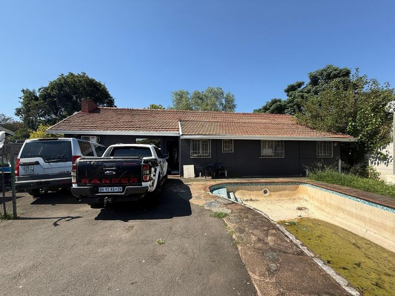 Rear exterior view of the house featuring a tiled roof, paved driveway, and a swimming pool in need of maintenance.