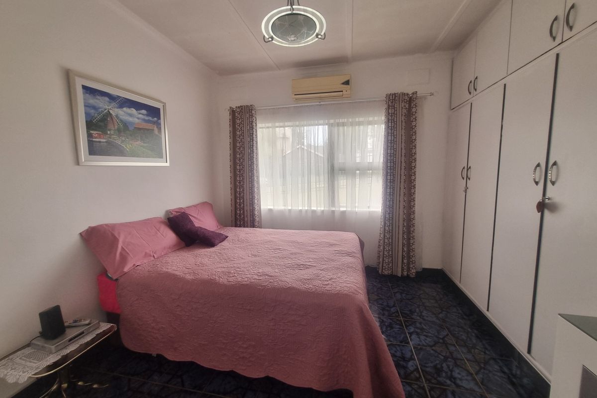 A functional bedroom featuring built-in cupboards, tiled flooring, and an integrated air conditioning unit.