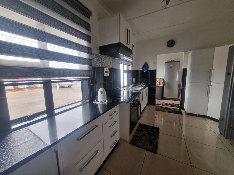 A functional kitchen featuring white cabinetry, dark granite countertops, tiled backsplash, and integrated appliances, with direct access to an adjacent utility area.