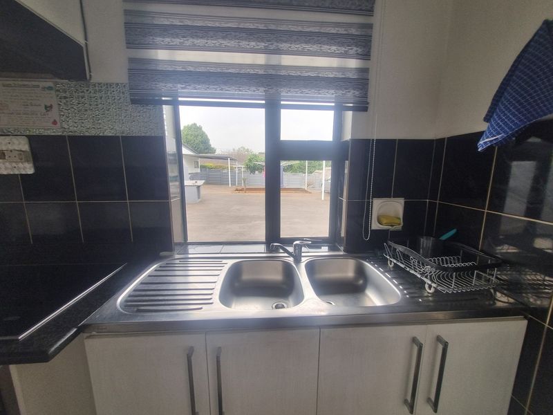 A functional kitchen area featuring a double bowl stainless steel sink, modern mixer tap, and dark tiled splashback with built-in cabinetry.