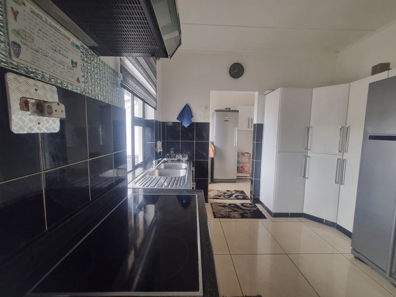 A functional kitchen featuring built-in white cabinetry, a black tiled backsplash, an electric hob with an extractor fan, and tiled flooring.