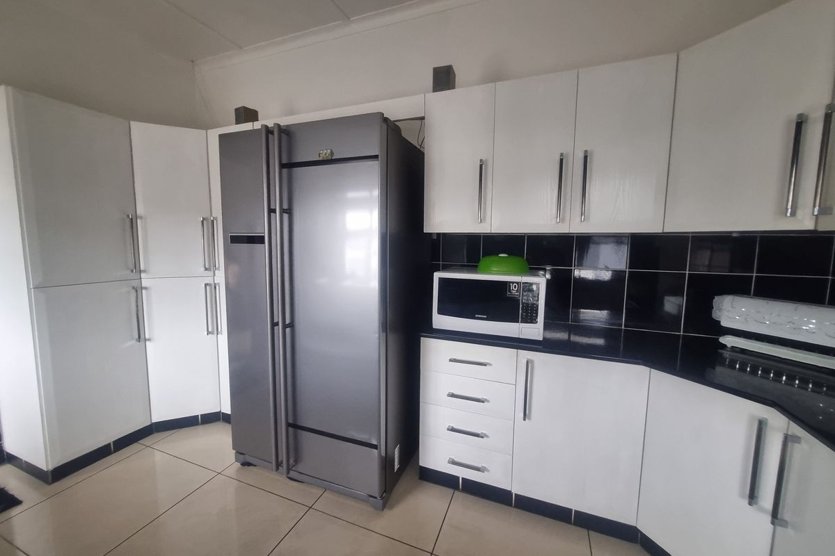 A functional kitchen featuring white cabinetry, black tiled backsplash, dark countertops, and tiled flooring.