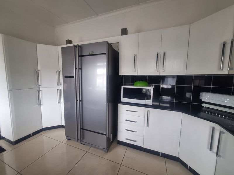 A functional kitchen featuring white cabinetry, black tiled backsplash, dark countertops, and tiled flooring.