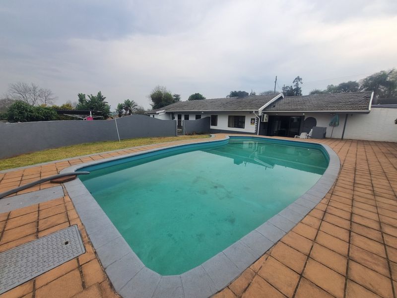Outdoor pool area featuring a swimming pool with tiled surround, boundary wall, and access to the main house structure.