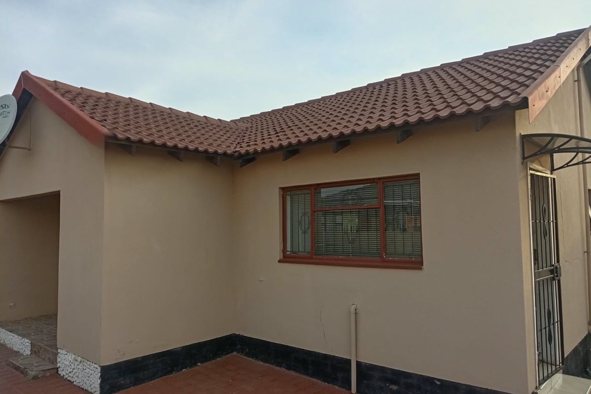 Rear exterior view of the house featuring a tiled roof, paved patio area, and secure entrance with a metal security gate.