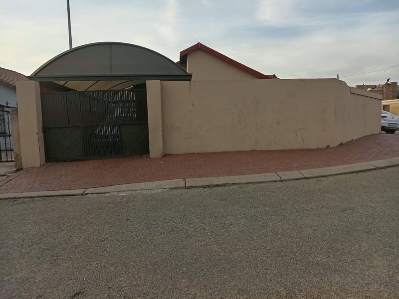 Front exterior view of the property featuring a perimeter wall, metal gate, and a covered carport area.