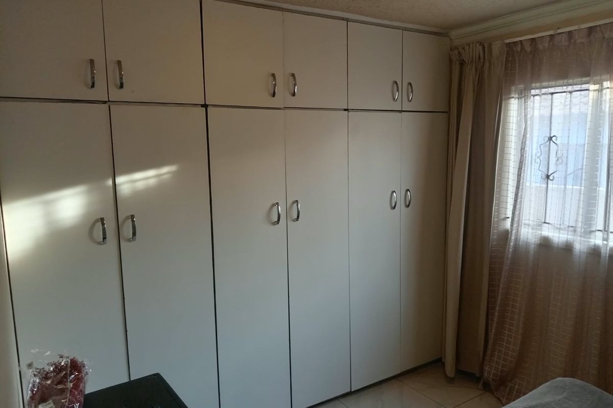 A bedroom featuring extensive floor-to-ceiling built-in cupboards, tiled flooring, and a window with security bars.