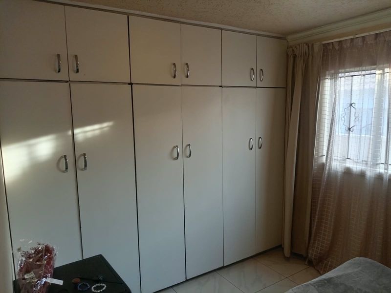 A bedroom featuring extensive floor-to-ceiling built-in cupboards, tiled flooring, and a window with security bars.