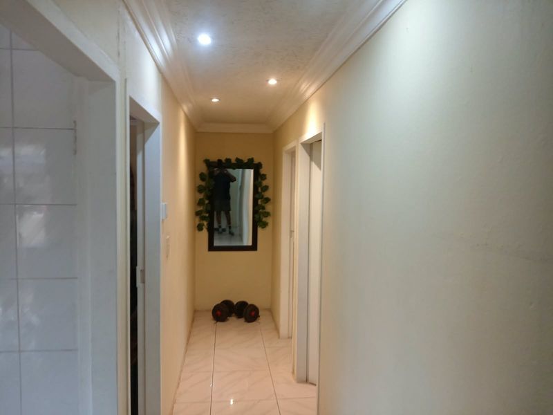 A well-lit hallway featuring tiled flooring, crown molding, and recessed downlights, providing access to multiple rooms.