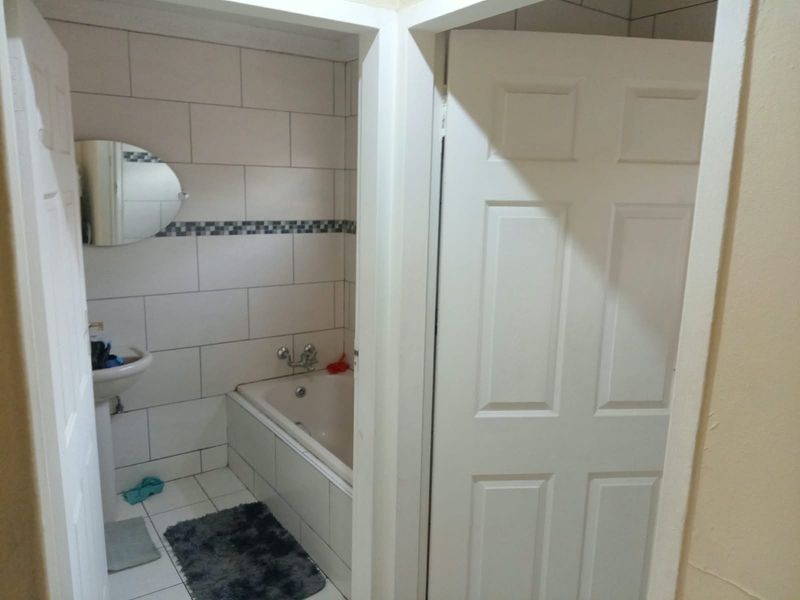 A functional bathroom featuring a built-in bathtub, pedestal basin, and neutral wall tiling, offering a clean and practical space.