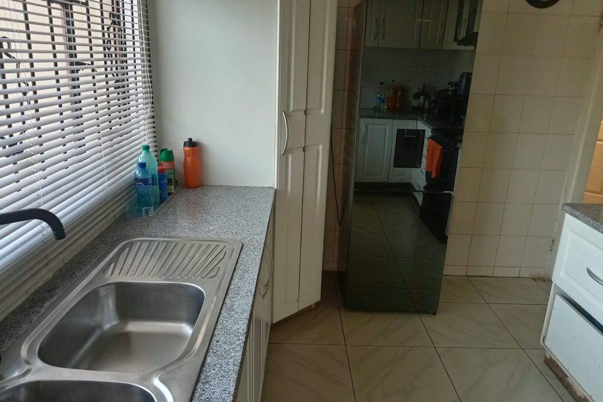 A functional kitchen featuring granite countertops, a double bowl stainless steel sink, tiled backsplash, and built-in cabinetry with tiled flooring.