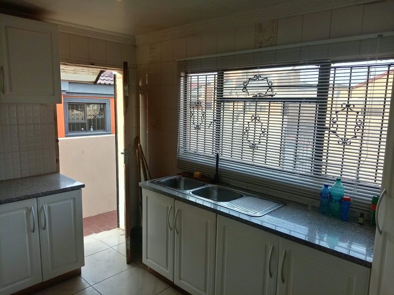 A functional kitchen featuring white cabinetry, granite countertops, a double bowl stainless steel sink, and tiled flooring with direct access to an outdoor area.