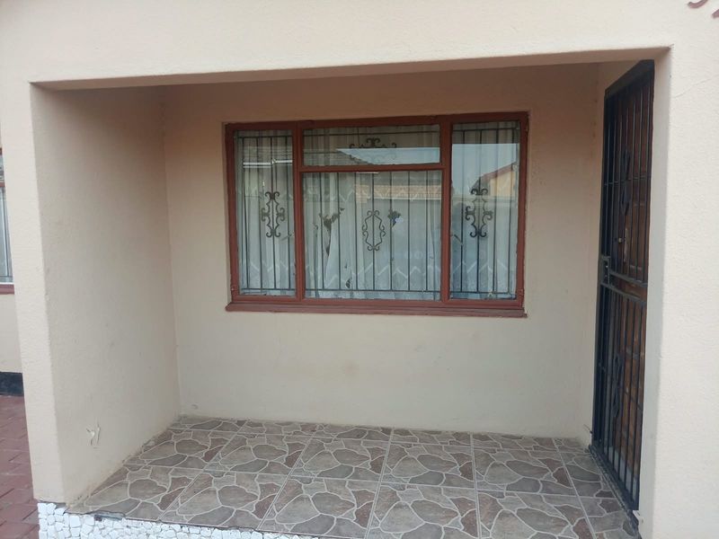 A covered entrance patio featuring tiled flooring, a security gate, and a window with security bars.