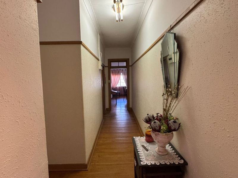 A traditional hallway featuring original hardwood flooring, picture rails, and a central ceiling light fixture, leading towards an adjacent room.