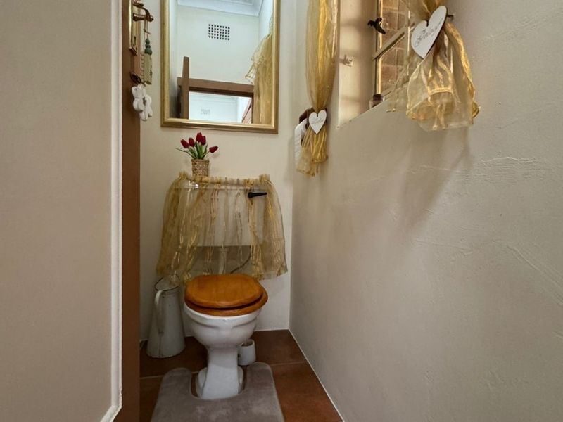A compact guest bathroom featuring tiled flooring, a standard toilet, and a wall-mounted mirror.